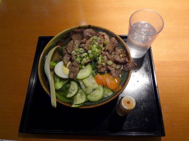 Bir bardak suyun yanında dilimlenmiş sebzeli bir kase biftek..