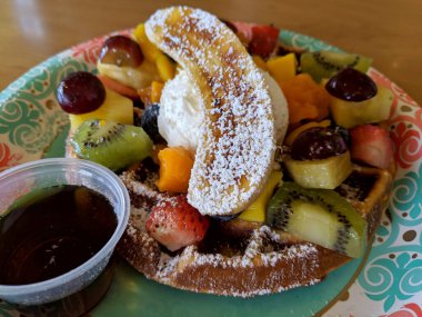 Taze meyve ve kremayla kaplı, şurupla servis edilen bir waffle..