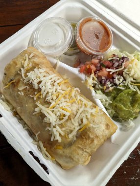 Cömertçe hazırlanmış bir paket Chimichanga dürümü üzerine dilimlenmiş peynir serpilir ve yanında salsa sosu, guacamole ve muhtemelen ekşi krema konserveleri bulunur. Hepsi de ahşap bir masaya konmuş köpük bir konteynırın içine yerleştirilir.