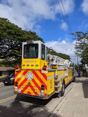 Waikiki - 4 Kasım 2021: Sarı ve kırmızı HFD itfaiye merdiven kamyonu şehir sokağının kenarına park edilmiştir. Kamyon 6 numara ile işaretlenmiş ve yansıtıcı güvenlik desenleri var. Az bulutlu açık mavi bir gökyüzü parlak bir ba sağlar.