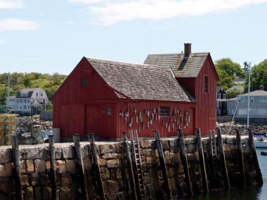 Rockport - June, 6 2024: A red wooden building stands on a stone pier in Rockport, with a small boat in the water. clipart