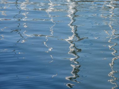 Suyun sakin yüzeyi yakındaki yapıların büyüleyici yansımalarını sergiliyor, ışık dalgaların üzerinde dans ederken dinamik bir desen oluşturuyor..