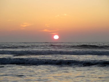 Güneş sakin okyanus dalgalarının üzerinde batarken ufuk sıcak renklerle parlıyor. Akşamları sahilde huzurlu bir atmosfer yaratıyor..