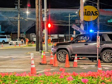 Honolulu - 26 Eylül 2024: Polis memurları, trafik ışıklarının altında yoğun bir Dillingham kavşağındaki trafiği yönetirken, arabalar kırmızı ışıkta duruyor, hayat dolu çiçekler yolu kaplıyor.