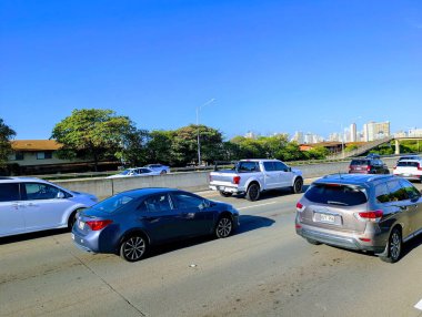 Honolulu - 12 Şubat 2025: Araçlar Oahu, Hawaii 'de parlak mavi bir gökyüzü ve ılık bir güneş altında, canlı ada yaşamını gösteren H-1 otobanı boyunca yol alırlar..