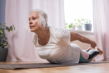 Evde tek başına pilates yapan yaşlı bir kadın.