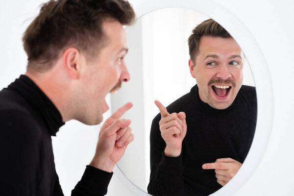 Молодой кавказский мужчина пытается взбодриться перед первым свиданием, глядя в зеркало