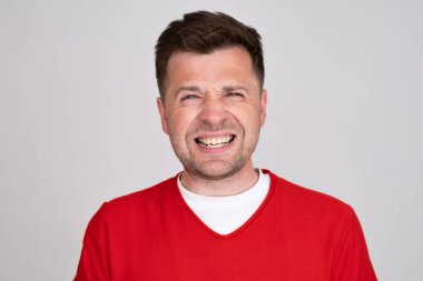 Kırmızı tişört giymiş kafası karışmış bir adam haberleri bekliyor. Kameraya şüpheyle bakıyor. Stüdyo çekimi. İnsani duygu.