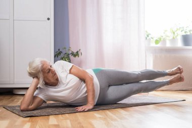 Evde tek başına pilates yapan yaşlı bir kadın.