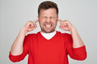 Stresli genç adam parmaklarıyla kulaklarını tıkayıp gözlerini kapalı tutuyor. Stüdyo çekimi 