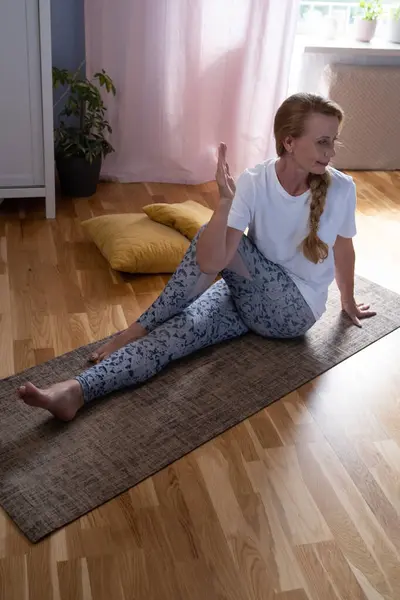 stock image Mature caucasian woman doing twisted yoga pose training at home. Healthy life concept