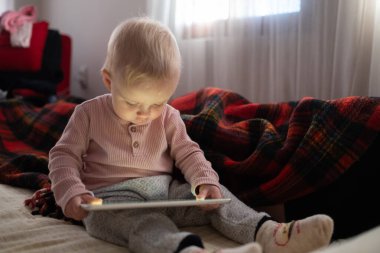 Küçük kız evdeki koltukta dijital kablosuz tabletle oynuyor. Çocuk ve elektronik aygıtlar kavramı. 