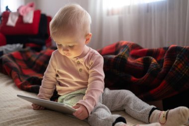 Küçük kız evdeki koltukta dijital kablosuz tabletle oynuyor. Çocuk ve elektronik aygıtlar kavramı. 