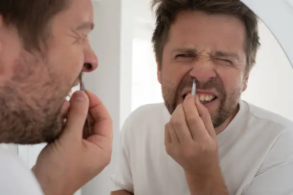 stock image Close up portrait of a suffering bearded man plucking out his nose hair.