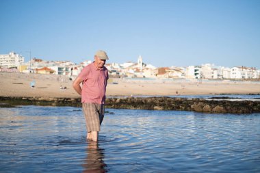 Kumsalda yürüyen bıyıklı yaşlı bir adam. 