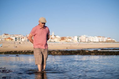 Kumsalda yürüyen bıyıklı yaşlı bir adam. 