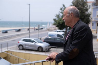 Portekiz 'de yürüyen ve okyanusa bakan yaşlı bir İspanyol. Ceket giyiyor ve bıyığı da var. Yüksek kalite fotoğraf