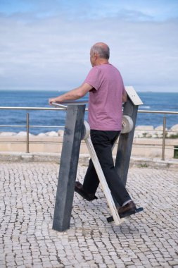Dışarıdaki Spor Salonu Aletleri 'nde Egzersiz Yapan ve Okyanusa Bakan Yaşlı Adam. Sağlıklı yaşam tarzı. Yüksek kaliteli illüstrasyon