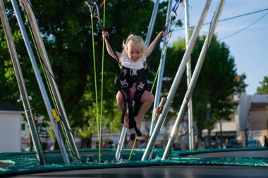 Emniyet kemeriyle trambolinde zıplamayı öğrenen küçük Avrupalı kız. Yaz Eğlencesi. Yüksek kalite fotoğraf