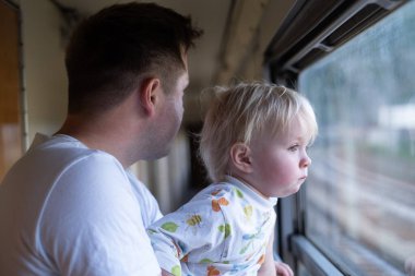 Genç adam babası, küçük çocuğuyla trenle geziyor, pencereye bakıyor.. 