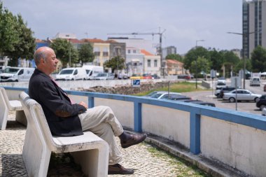 Portekiz 'in küçük bir kasabasında bir bankta oturan spor ceketli yaşlı İspanyol adam sahile bakıyor. Yüksek kalite fotoğraf