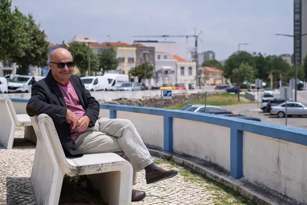 Portekiz 'in küçük bir kasabasında bir bankta oturan spor ceketli yaşlı İspanyol adam sahile bakıyor. Yüksek kalite fotoğraf