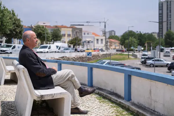 Portekiz 'in küçük bir kasabasında bir bankta oturan spor ceketli yaşlı İspanyol adam sahile bakıyor. Yüksek kalite fotoğraf