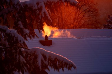 Sonnenuntergang beleuchtet die verschneiten Daecher, ein dampfender  Kamin sorgt fuer Stimmung