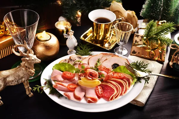 一盘切好的火腿和烤好的肉 放在有金色装饰的黑桌上过圣诞节 — 图库照片