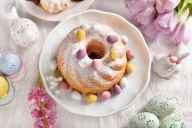 Top view of traditional Easter ring cake sprinkled with powdered sugar and candy eggs on festive table 
