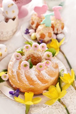 Easter table with homemade ring cake sprinkled with powdered sugar and muffins with sugar decors in pastel colors