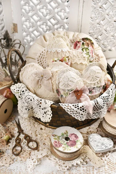 复古风格依旧存在 篮子里塞满了手工制作的心脏 枕头上缝着亚麻布和花边 铺在白色的木制桌子上 — 图库照片