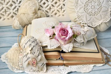 Açılan eski kitaplar, güller, eski el yapımı kalpler ve masanın üzerinde duran bir yastıkla romantik bir düzen.