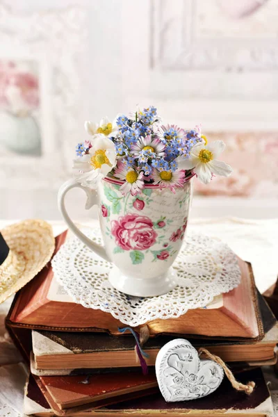 瓷杯中的一束雏菊和淡忘的花朵矗立在一堆翻开的旧书上 它们都是老式的内饰 — 图库照片