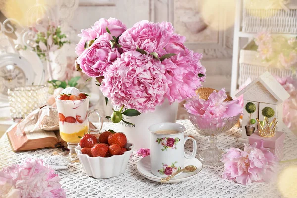 Shabby chic style interior with strawberry dessert, coffee and bunch of pink peonies on the table