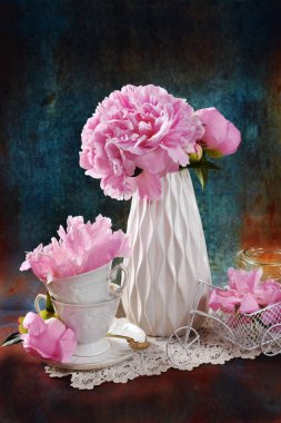 Seramik vazoda pembe şakayıklar ve grunge fonda porselen bardaklarla dolu bir hayat. 