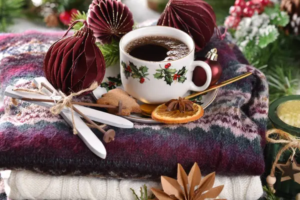 Winter coffee on stack of colorful woolen sweaters with burgundy paper ornaments and miniature ski decor