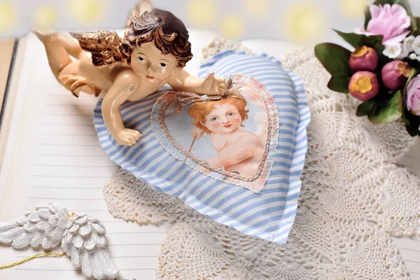 Angel figurine and handmade white and blue striped heart decor lying on opened book