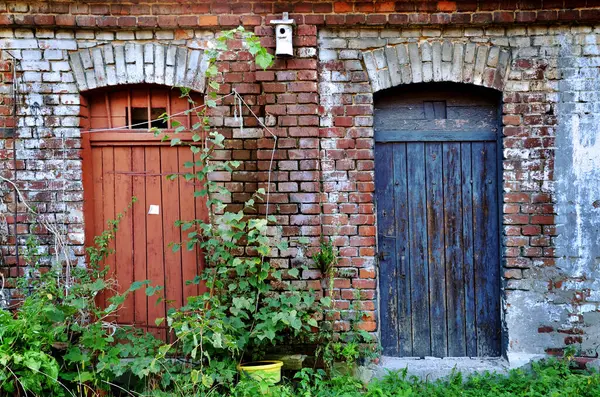 stock image Brick building with two old doors in red and blue color of lumber-rooms or shed