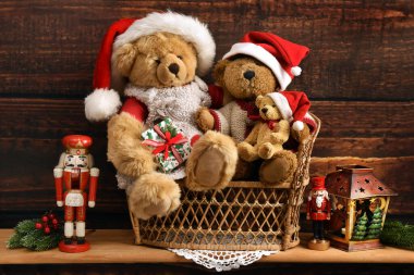 Wooden shelf with Christmas decorations and teddy bear family in Santa's hat sitting on wicker sofa 