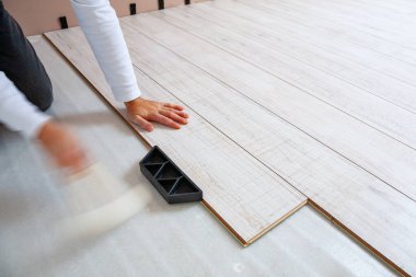 Bir inşaat işçisi yeni lamine döşeme döşemesi kuruyor ve plastik bir çekiçle döşeme tahtasına çarpıyor.