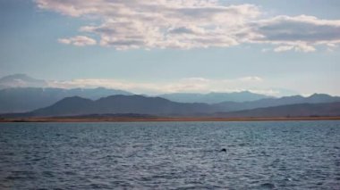 Blue calm water in Issyk-Kul lake with mountains on background at summer day, realtime footage.