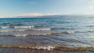 Blue calm water in Issyk-Kul lake with mountains on background at summer day, realtime footage.