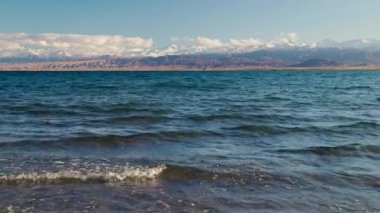 Blue calm water in Issyk-Kul lake with mountains on background at summer day, realtime footage.