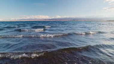 Blue calm water in Issyk-Kul lake with mountains on background at summer day, realtime footage.