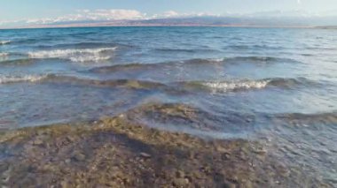 Small vawes of Issyk-Kul lake with mountains on background at summer day, ultra-wide angle close-up realtime footage.