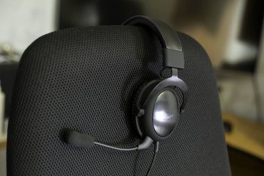 Boş bilgisayar sandalyesinin arka koltuğunda hava örgüsü döşeli siyah kulaklık..