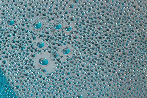 water drops on aurora green pearl glass of modern phone back cover, close-up with selective focus.