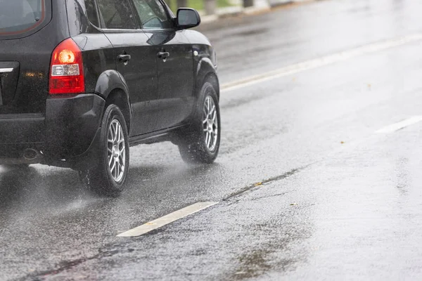 rain water splash flows from wheels of black car that moving fast on asphalt road.