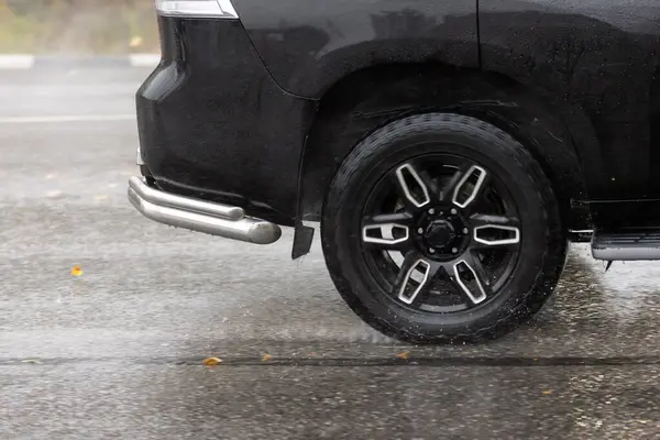 rain water splash flows from wheels of black SUV that moving fast on asphalt road.
